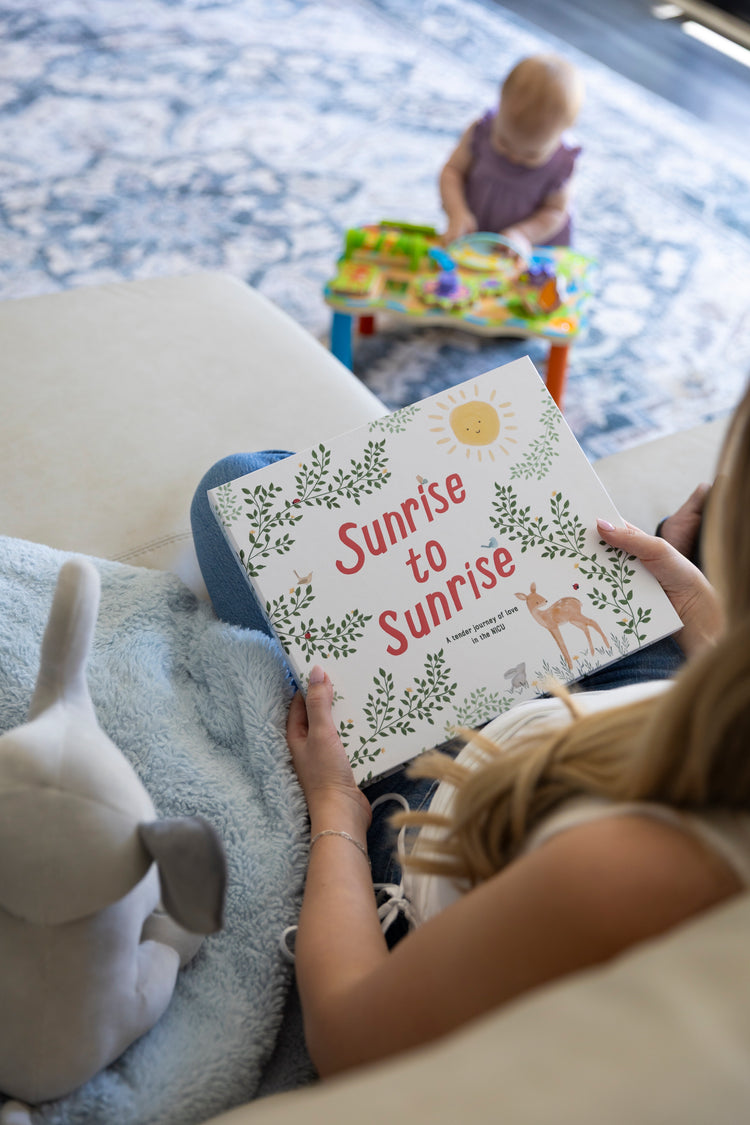 Mom reading Sunrise to Sunrise NICU memory book with toddler playing in background